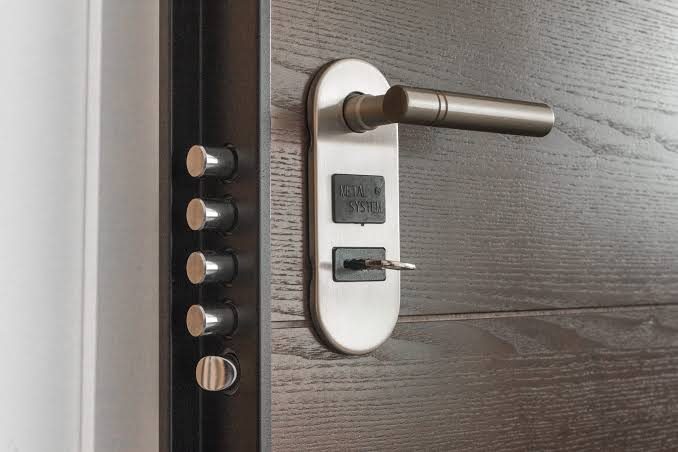 Close-up of a multi-point security door lock and handle fitted to a wooden door, showing the bolt mechanism and lock cylinder